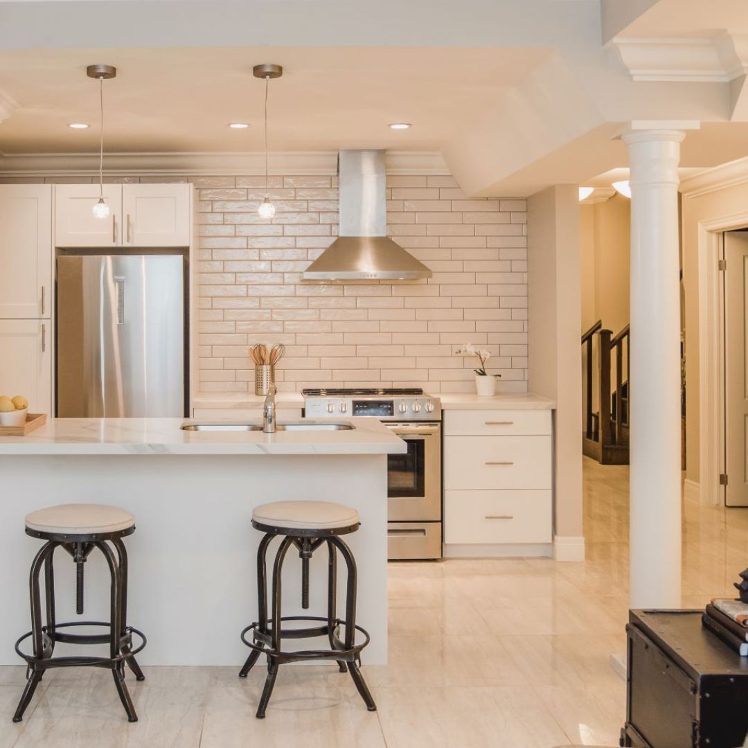 Open concept kitchen and living area with white cabinets, kitchen island, and bar stools. Pendant lights add style over the countertop.