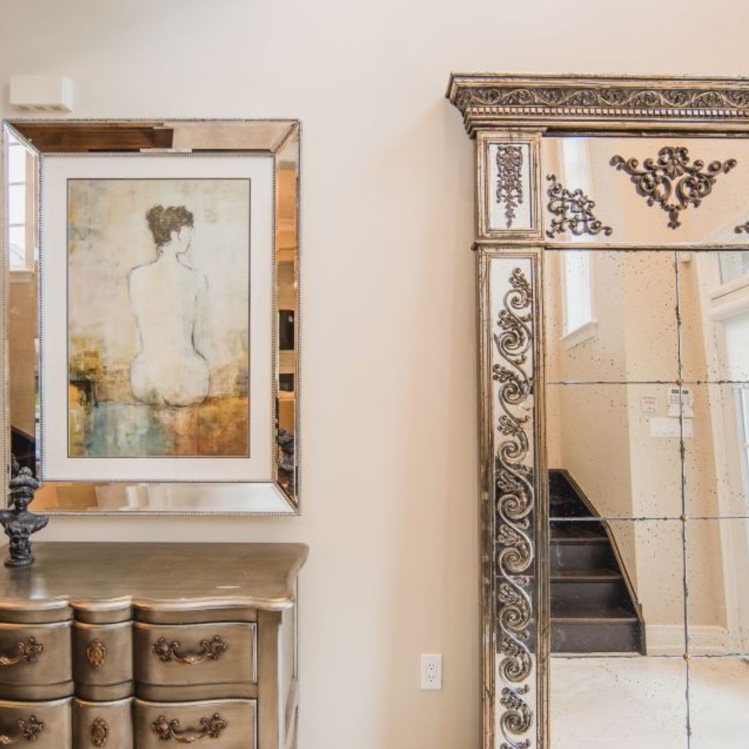 Sophisticated foyer with gold-framed mirror and vintage-inspired chest. Framed figure painting adds artistic touch. Ornate mirror details and warm color palette create an inviting entrance.