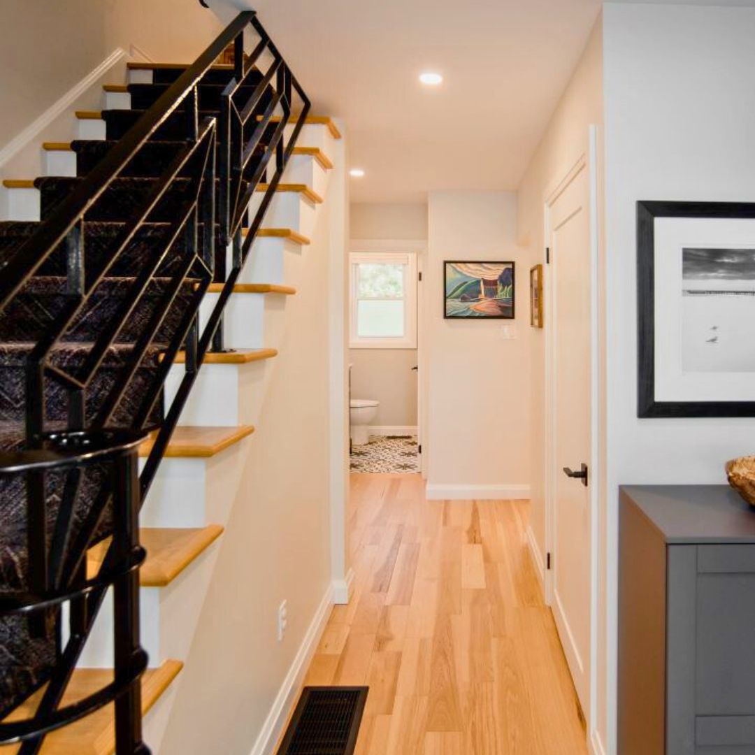 Modern hallway with black railing staircase, wood floors, and framed artwork on white walls