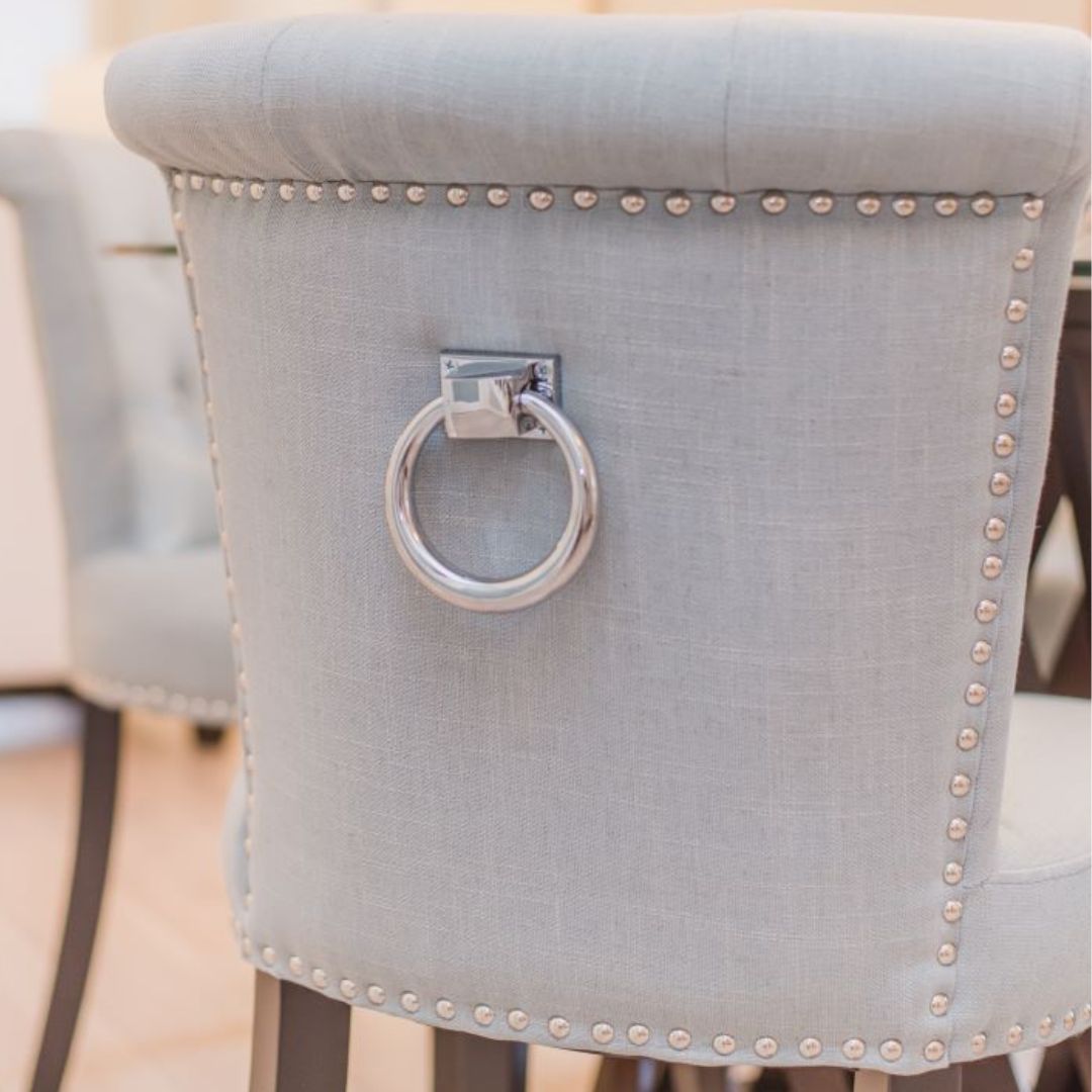 Close-up of light grey upholstered dining chair with silver ring pull and decorative nail trim 