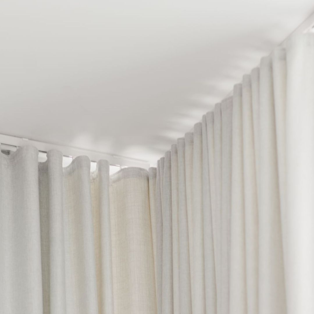 Close-up of a white ceiling-mounted curtain track with flowing cream-colored curtains, demonstrating a sleek window treatment solution.