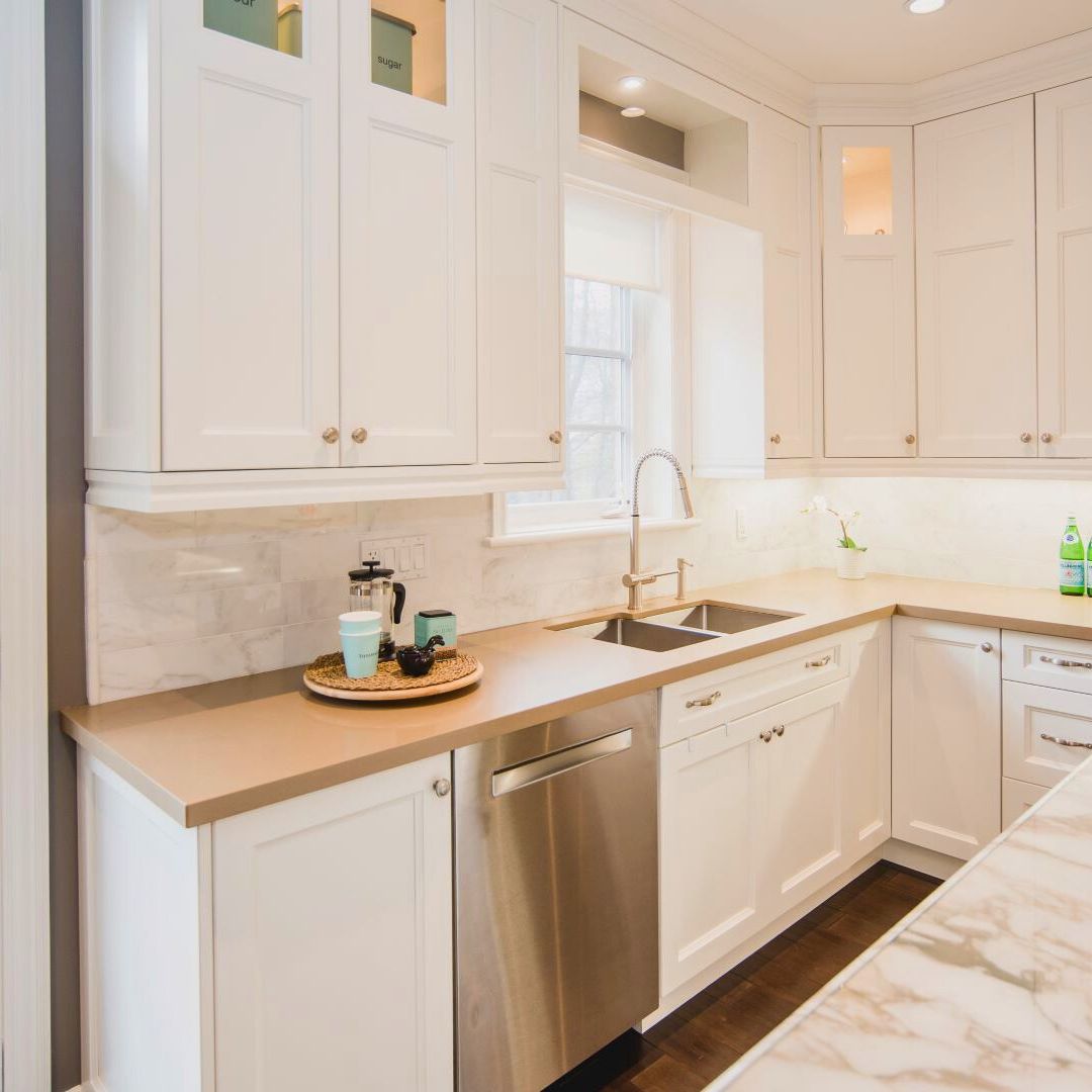 Bright white kitchen with custom cabinetry, stainless appliances, and marble countertops. Large window above sink lets in natural light.